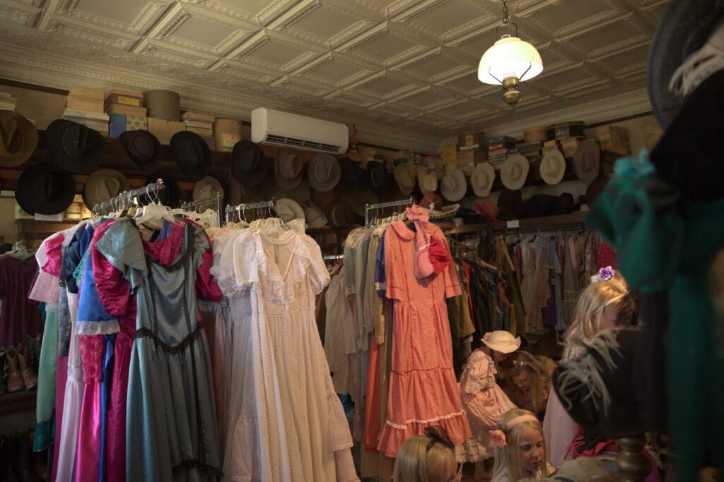 Young girls choosing accessories for their costume rentals in front of racks of clothes and hanging cowboy hats